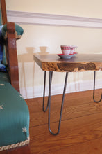 Load image into Gallery viewer,  live edge side or accent table comprised of black walnut slab with hand-forged hairpin legs for a cool mid-century modern look. Slab is hand finished and accented with a single cherry bowtie inlay